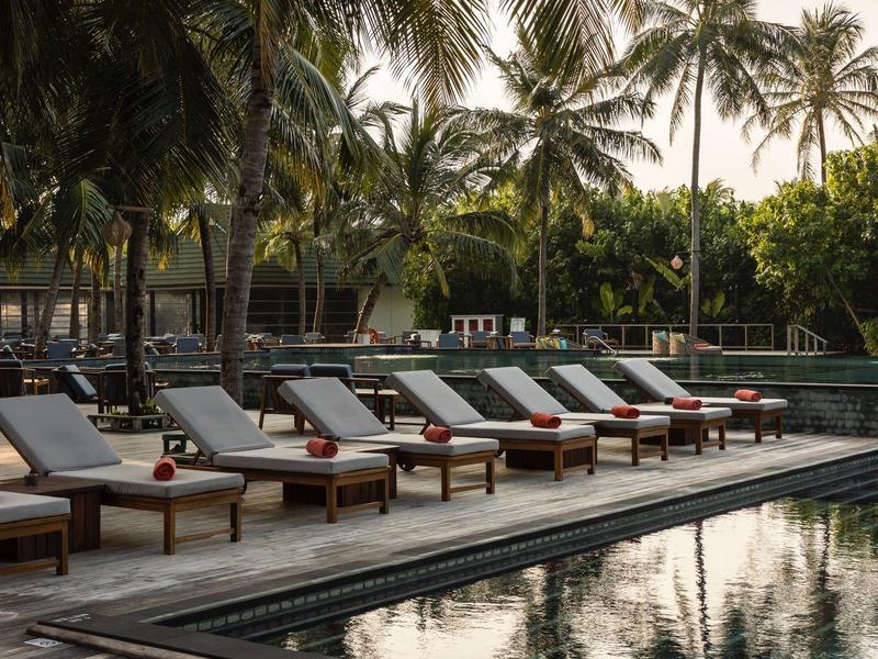 Entspannende Poollandschaft mit Liegestühlen und Palmen im Hintergrund.