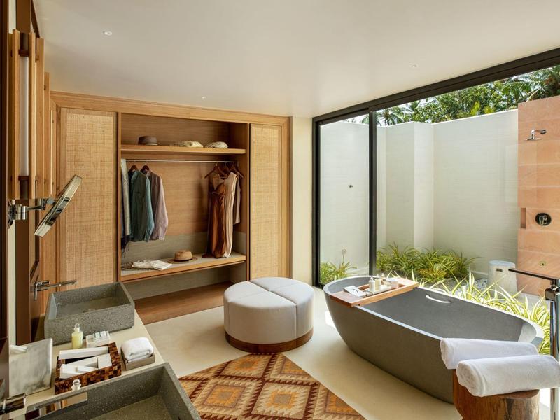 Modern bathroom with freestanding bathtub and garden view through large windows.