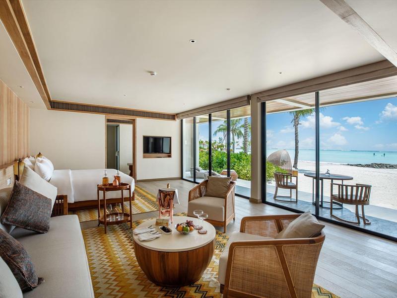 Modern hotel room with seating area and sea view through large glass windows.