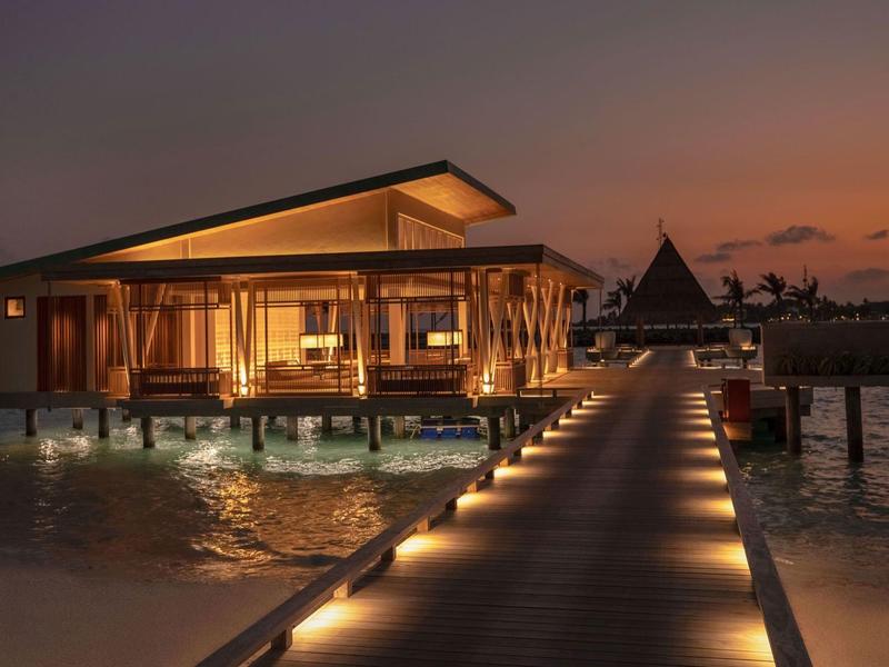 Luxury overwater bungalows with warm lighting and beach walkway at sunset.