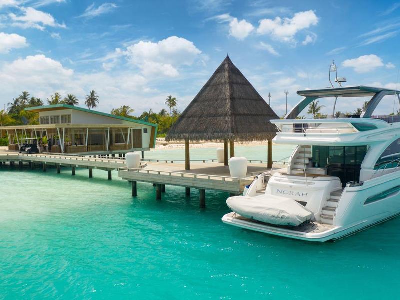 Luxury yacht moored at a pier with tropical beach and pavilion in the background