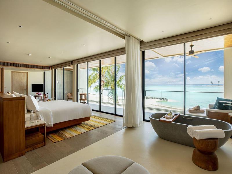Modern hotel room with large bed, ocean view, and seating area with two armchairs.