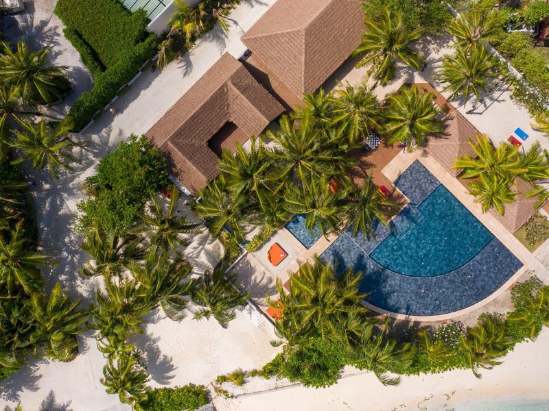 Vista aérea de un resort con piscina, palmeras y playa de arena blanca junto al mar.