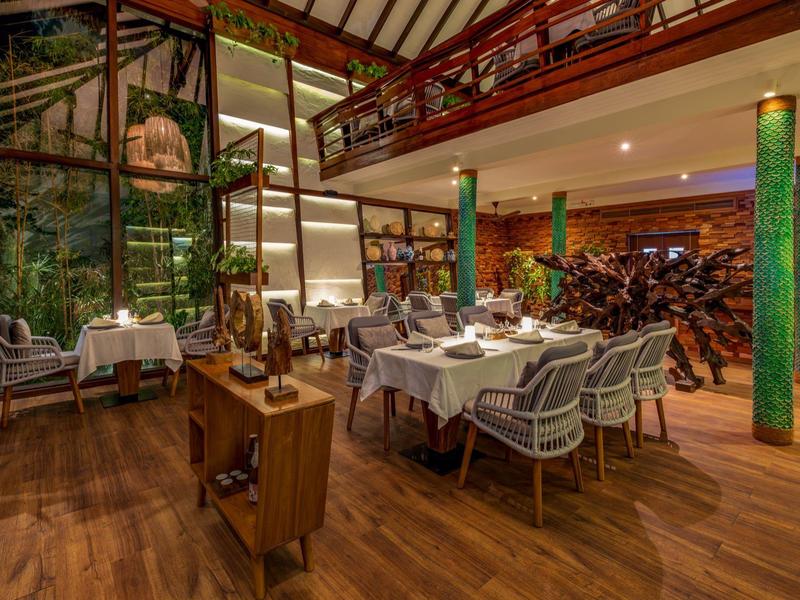 Interior elegante de restaurante con suelo de madera, mesas blancas y decoración verde.
