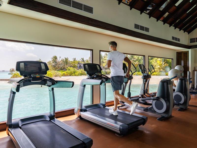 Gimnasio con grandes ventanas frente al mar y máquinas de correr con una persona entrenando.