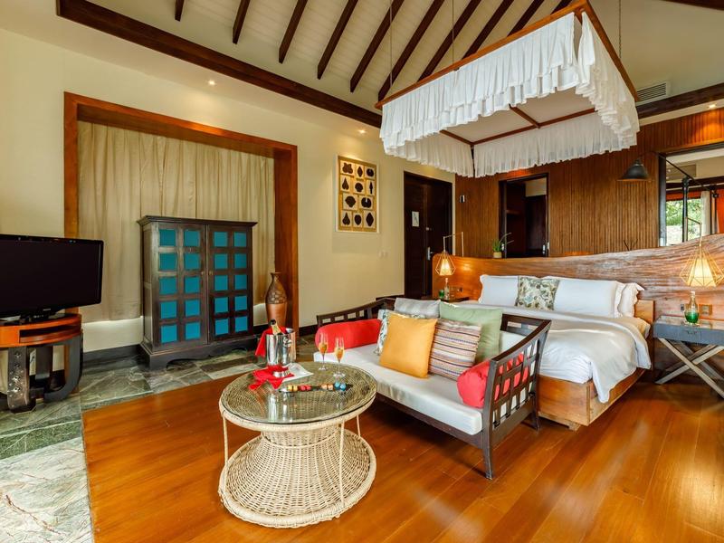 Acogedora habitación de hotel con suelo de madera, cama doble y área de estar con sofá y mesa de centro.