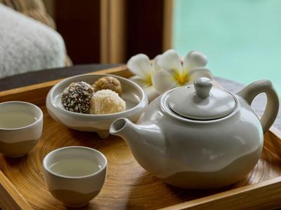 Teekanne, zwei Teetassen und Dessert auf einem Holztablett neben einem Schwimmbad.