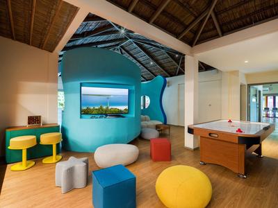 Innenansicht eines modernen Freizeitraums mit bunten Sitzmöbeln, Spieltisch und großer Glaswand.