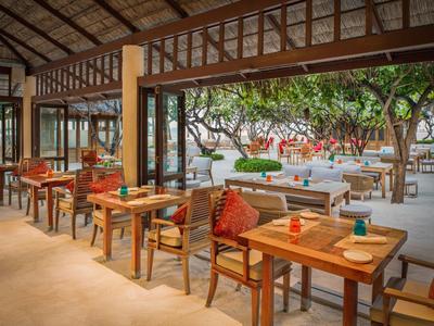 Offener Essbereich mit Holztischen und Stühlen, Blick auf Garten mit Bäumen und Loungebereich.