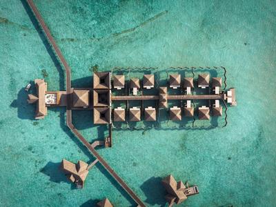 Luftaufnahme von Bungalows über klarem türkisfarbenem Wasser in einem Resort.