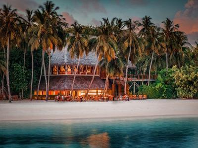 Ein tropisches Strandresort mit Palmen und beleuchteten Bungalows bei Sonnenuntergang.