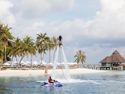 Persona su flyboard sopra l'acqua con palme e bungalow sulla spiaggia sullo sfondo