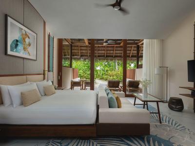 Modernes Hotelzimmer mit großem Bett, Sitzbereich und Blick auf eine Terrasse mit Garten.