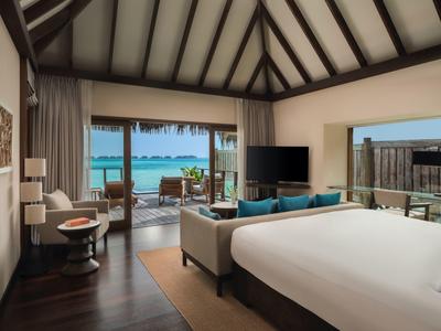 Modernes Hotelzimmer mit großem Bett, Sofa und Blick auf eine Terrasse am Wasser.