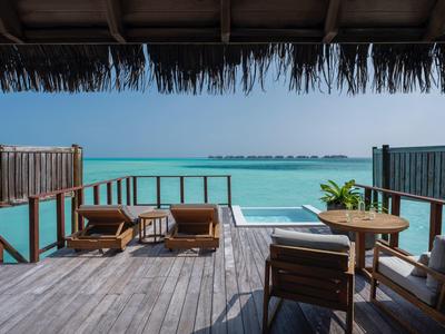 Terrasse mit Holzmöbeln und Blick auf das türkisfarbene Meer unter klarem Himmel.