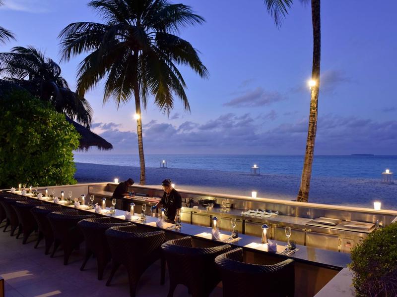 Abendliche Strandterrasse mit gedeckten Tischen und Palmen bei Dämmerung.