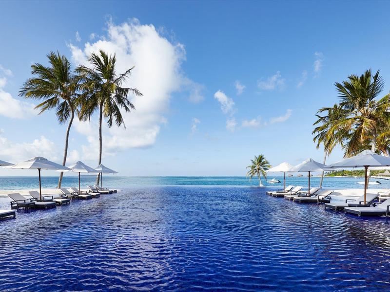 Infinity-Pool mit Blick auf den Ozean und Sonnenschirmen unter Palmen bei klarem Himmel.