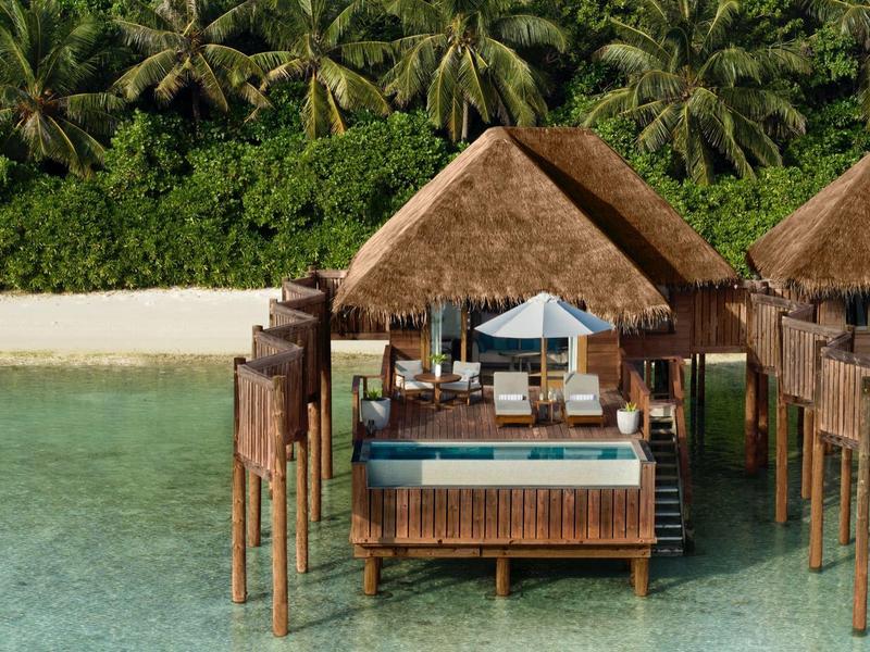 Überwasserbungalows mit privaten Pools an einem tropischen Strand mit Palmen.