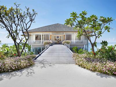 Elegante hotel su due piani con lungo vialetto e piante tropicali in primo piano.