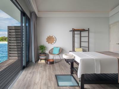 Camera moderna con lettino da massaggio, sedia e vista mare tramite grandi finestre scorrevoli.