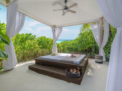 Padiglione aperto con letto e vista sul mare, circondato da piante verdi.
