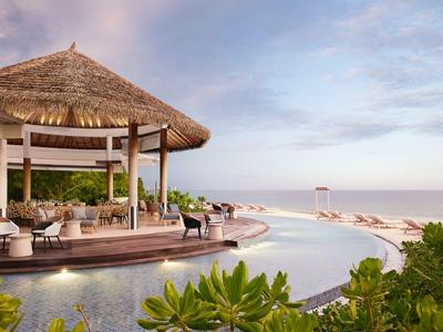 Zone de piscine luxueuse avec coin salon au toit de chaume et vue sur la plage.