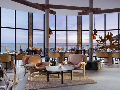 Restaurant moderne avec grandes fenêtres et vue sur la mer au coucher du soleil.