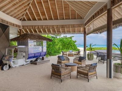 Espace lounge ouvert avec chaises en bois et tables sous des toits de chaume dans une station balnéaire.