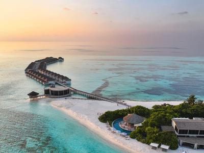 Vista di resort su un atollo tropicale con moli e acqua limpida al tramonto.