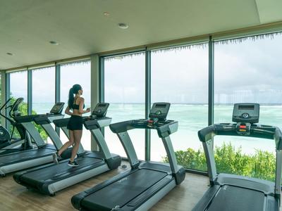 Salle de sport moderne avec tapis de course et vue sur l'océan à travers de grandes fenêtres.