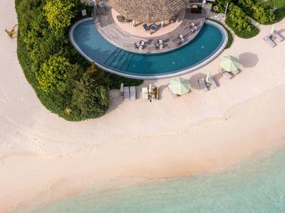 Ristorante rotondo sulla spiaggia con piscina, circondato da sabbia e acqua limpida.