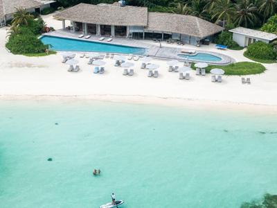 Resort sulla spiaggia con sabbia bianca, piscina e ospiti in acqua turchese.