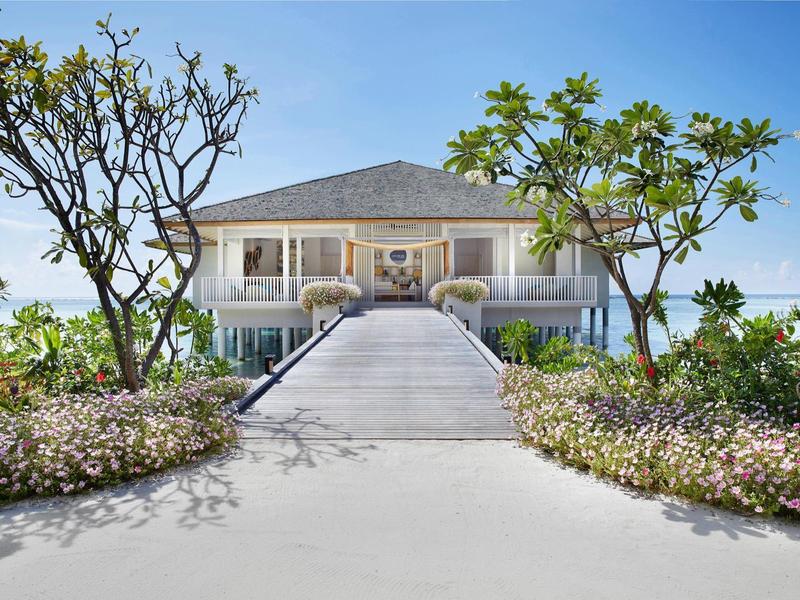 Elegante hotel su due piani con lungo vialetto e piante tropicali in primo piano.