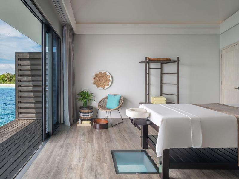 Camera moderna con lettino da massaggio, sedia e vista mare tramite grandi finestre scorrevoli.