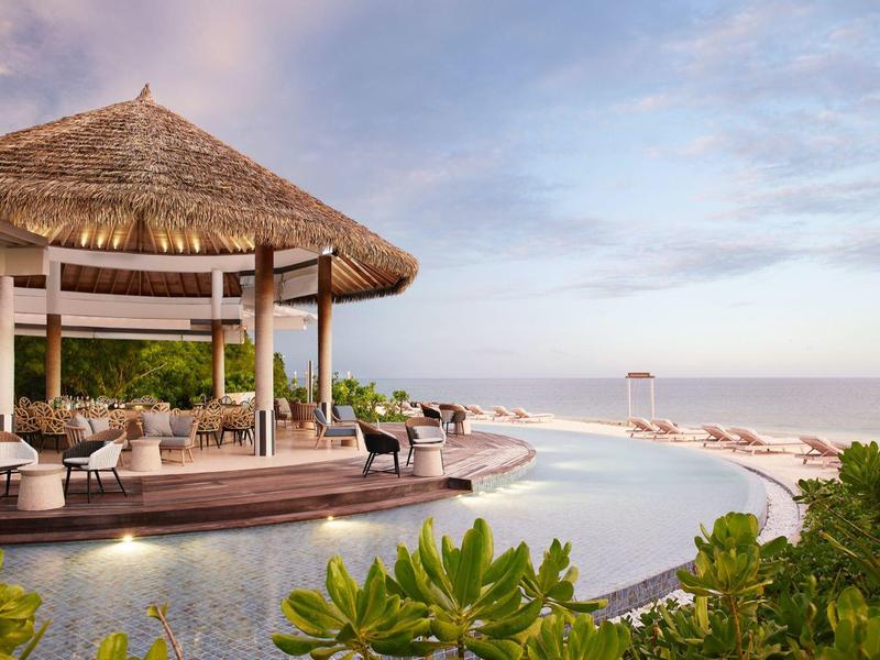 Zona piscina di lusso con vista sulla spiaggia e sul mare turchese sotto un cielo nuvoloso.