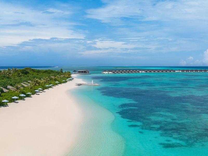 Spiaggia di sabbia bianca con ombrelloni verdi e mare turchese chiaro sotto cielo blu
