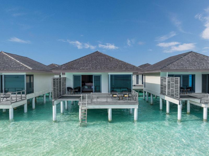 Bungalow su palafitte sopra acqua tropicale limpida sotto un cielo blu.