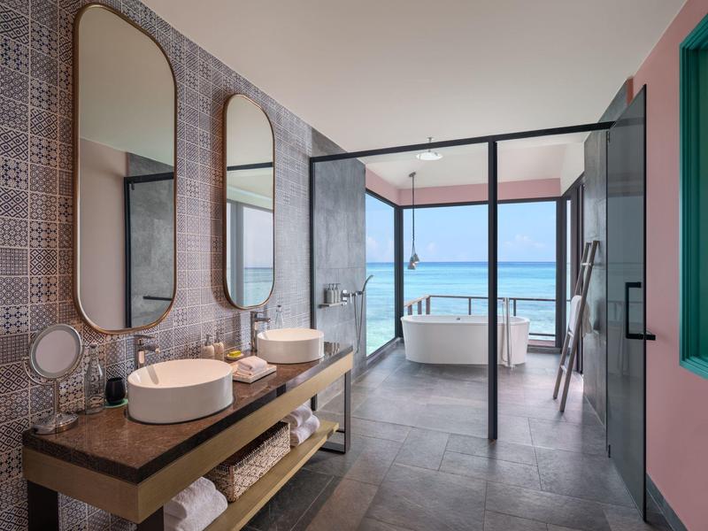 Bagno moderno con parete in vetro, vasca autoportante e doppio lavabo con vista sul mare.