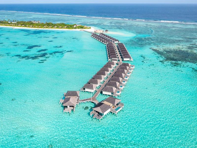 Bungalow su palafitte in acqua turchese con isola sullo sfondo.