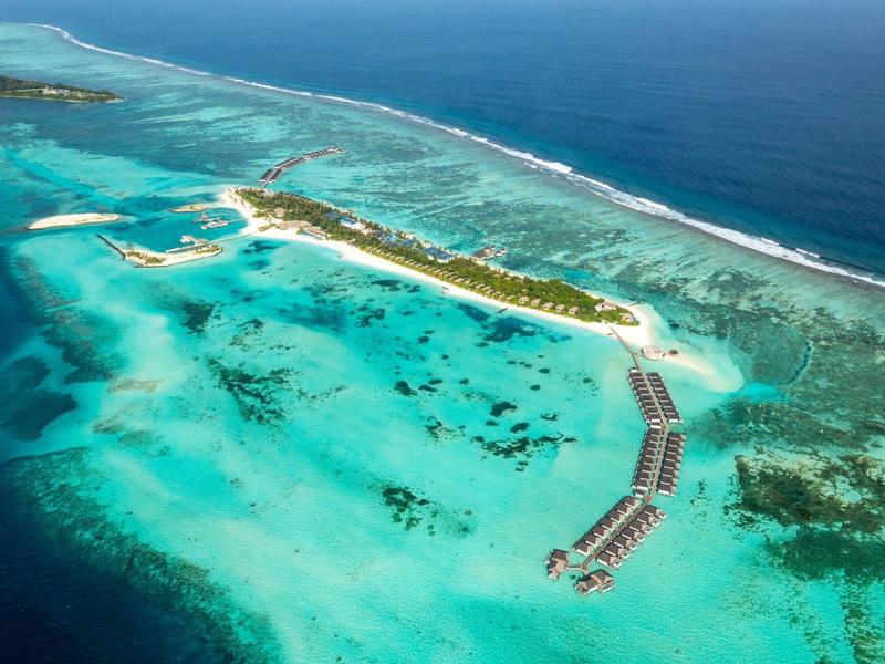 Veduta aerea di un'isola tropicale con acqua turchese e bungalow sull'acqua.