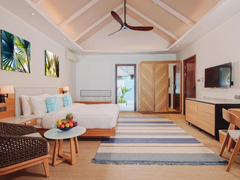 Helles Schlafzimmer mit Holzdecke, großem Bett, Teppich, Holzstuhl und Möbeln in warmen Tönen.