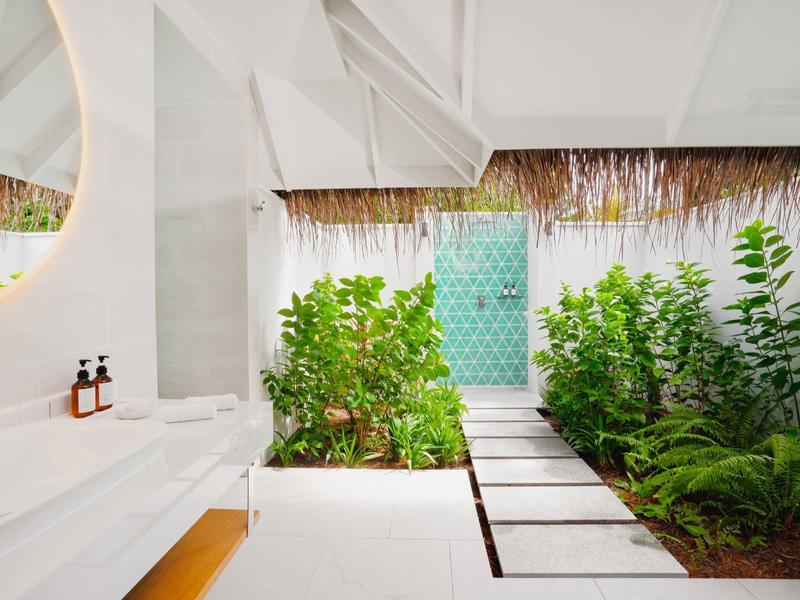 Moderner Innenhof mit großem Blumengarten, weißem Boden und türkisfarbener Tür im Hintergrund.