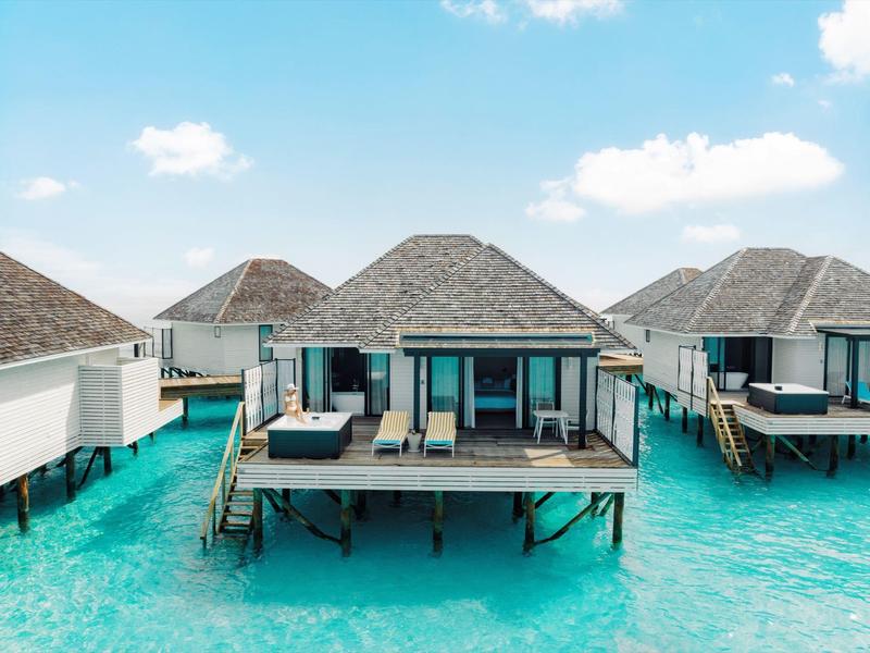 Überwasserbungalows mit Holzkonstruktion und Strohdächern auf türkisblauem Wasser unter blauem Himmel.