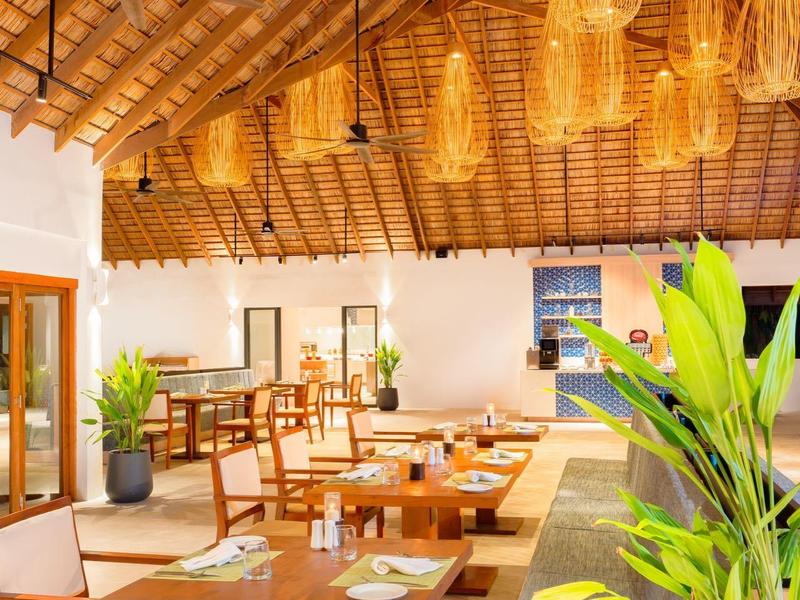 Modernes Restaurant mit Holzdach, hängenden Lampen und Holzstühlen an rechteckigen Tischen.