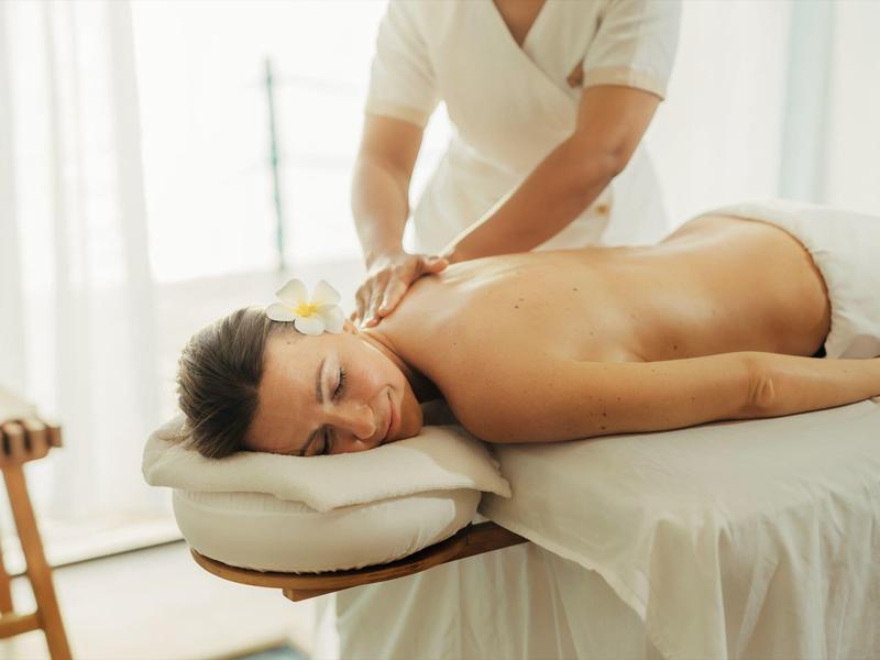 Frau liegt entspannt auf Massagebank, während Therapeutin ihre Schultern massiert in hellem Raum.