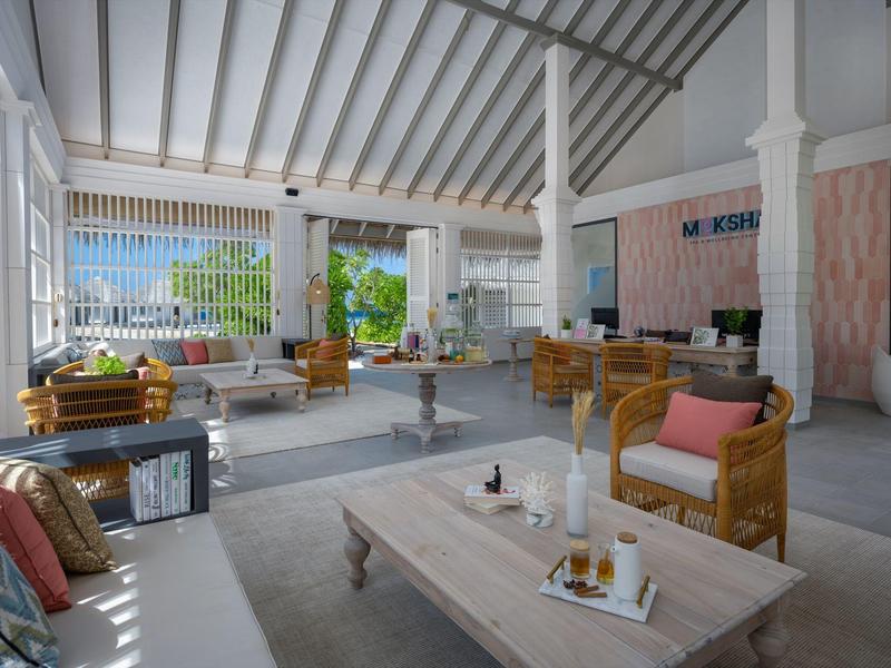 Amplio lobby de hotel con muebles de madera, cojines coloridos y luz natural que entra por grandes ventanales.