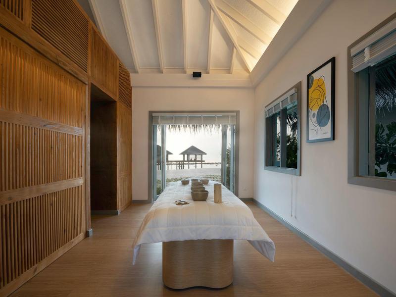 Pasillo moderno de hotel con mesa de reuniones, techo de madera y vista a un pabellón en el mar.