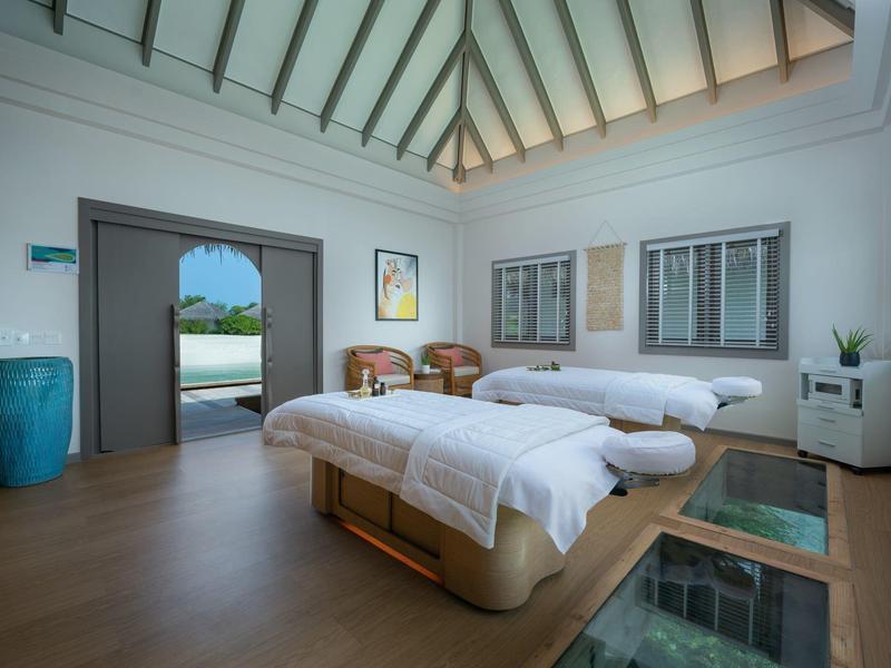 Sala de spa moderna con dos camillas de masaje y vista al área exterior.