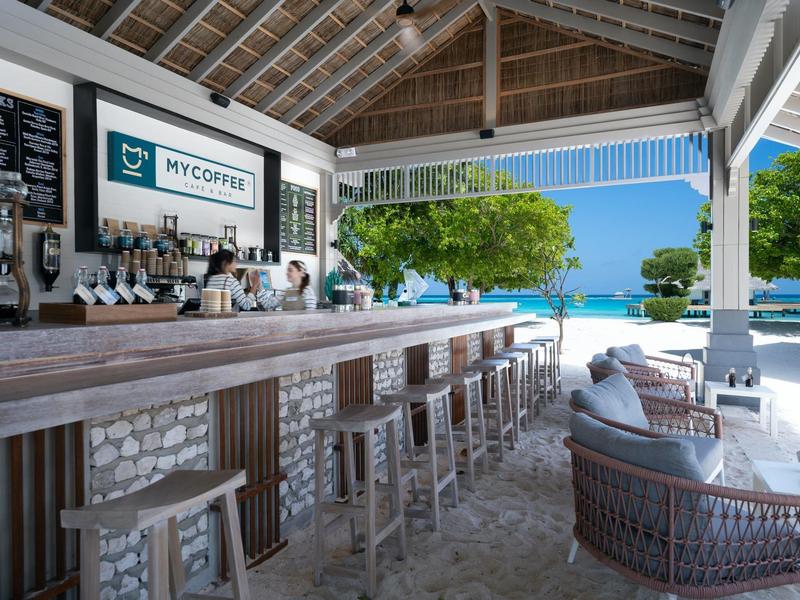 Área exterior moderna con bar y asientos cerca del mar y la playa bajo techo de madera.