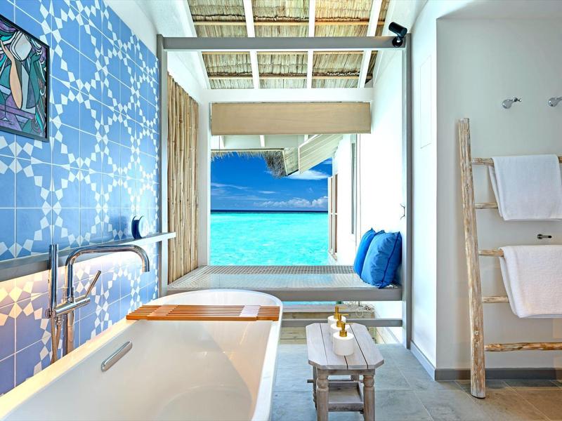 Oasis de bienestar luminosa con bañera, decoración azul en la pared y vista al mar.